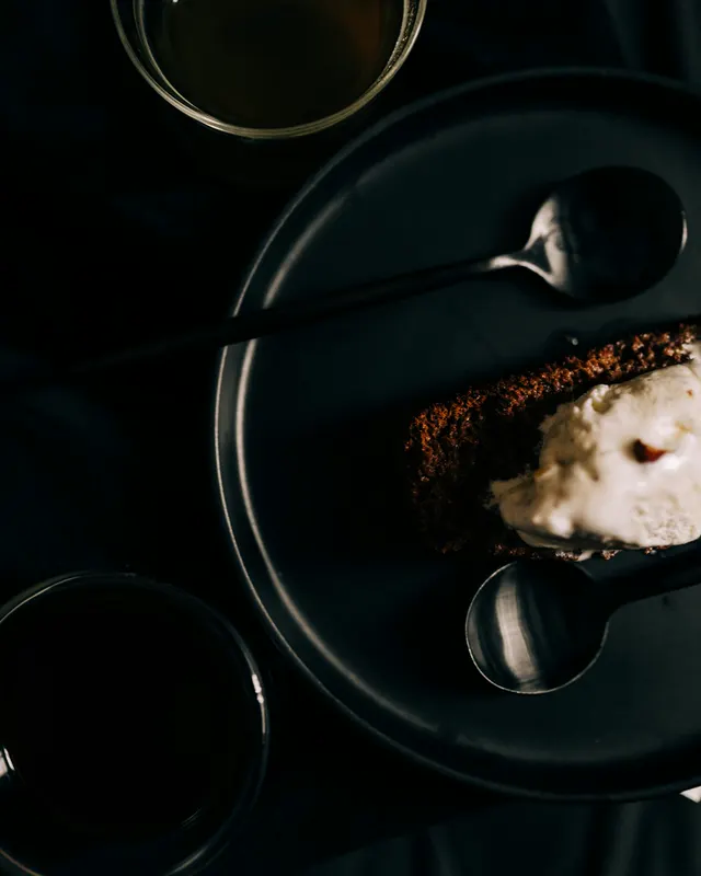 Dunkles Dessert mit Rauchsahne auf schwarzem Teller, daneben Espresso